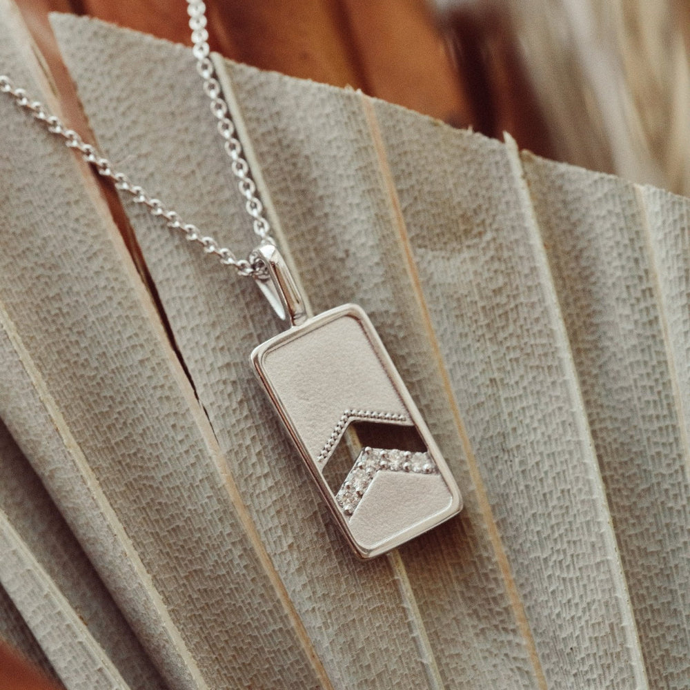 A 14k gold necklace with a rectangle pendant and round pave diamonds, displayed on a rolo chain.