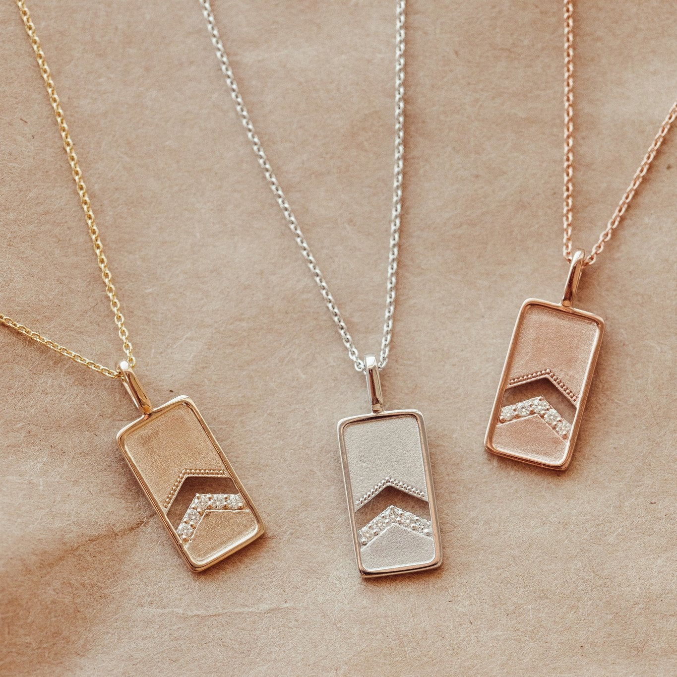 A 14k gold necklace with a rectangle pendant and round pave diamonds, displayed on a rolo chain in white, rose, and yellow gold