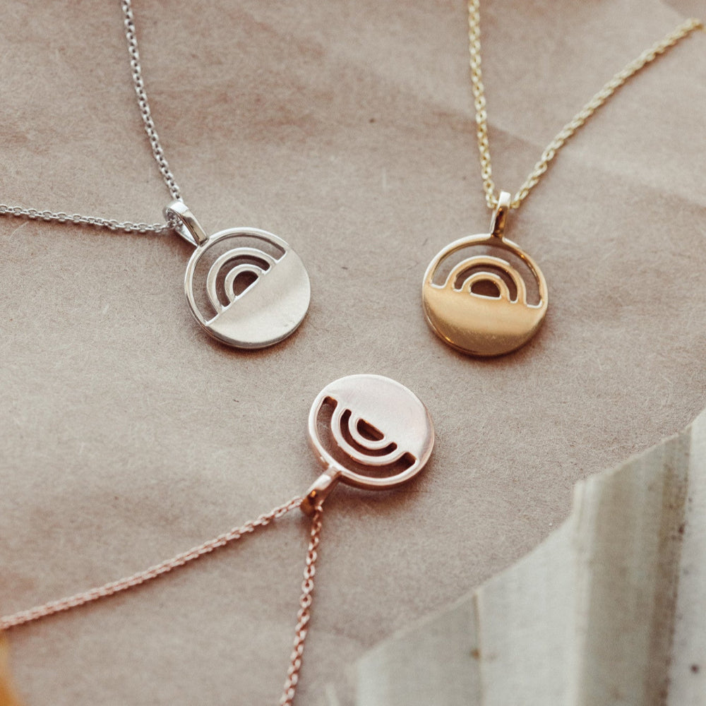 Three necklaces with circular pendants on a textured surface in 14k white, yellow, and rose gold