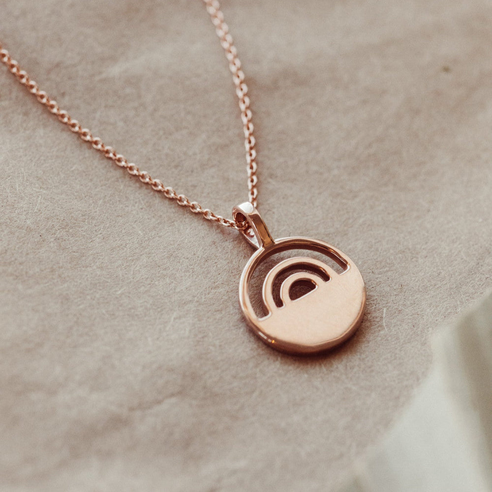 Rose gold necklace with a round pendant on a beige fabric background