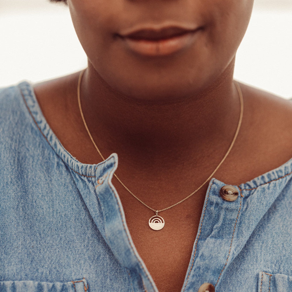 Person wearing a gold necklace with a pendant, close-up of the neck and denim shirt.
