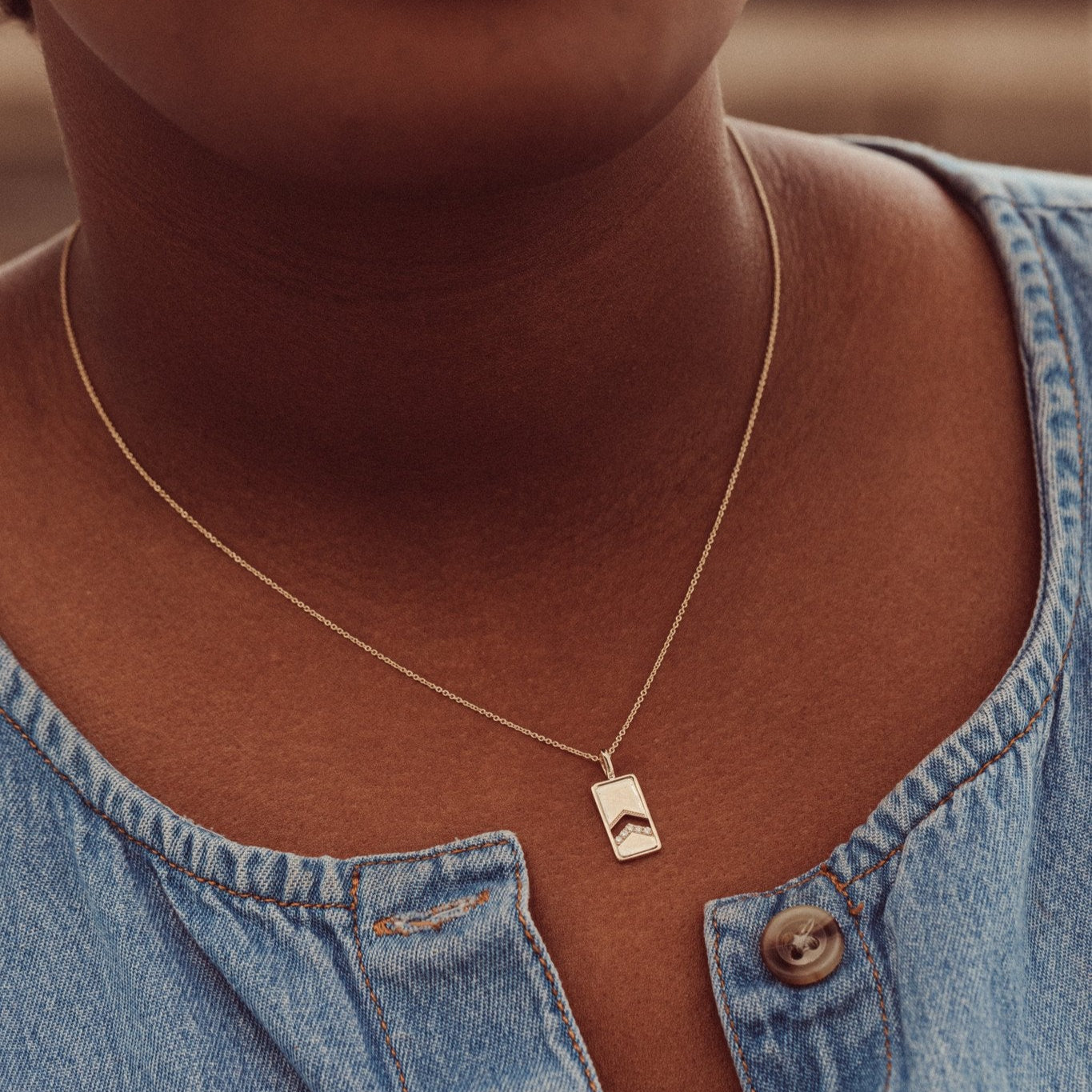 A 14k gold necklace with a rectangle pendant and round pave diamonds, displayed on a rolo chain on a models neck