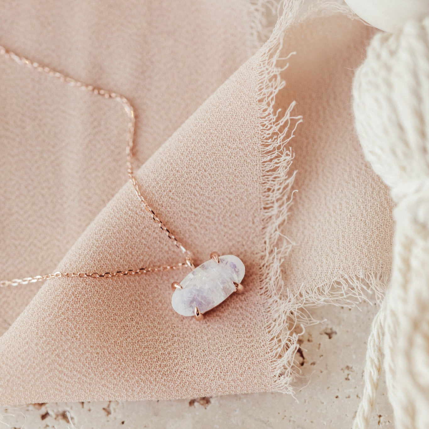 A large oval moonstone necklace in prongs set east/west on a 16"-18" adjustable chain, displayed on a pink fabric surface.