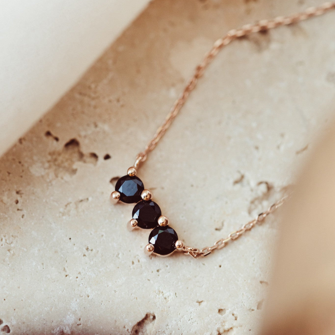 A 14k gold necklace featuring three round black spinel stones set in prongs, displayed on a piece of jewelry stand.