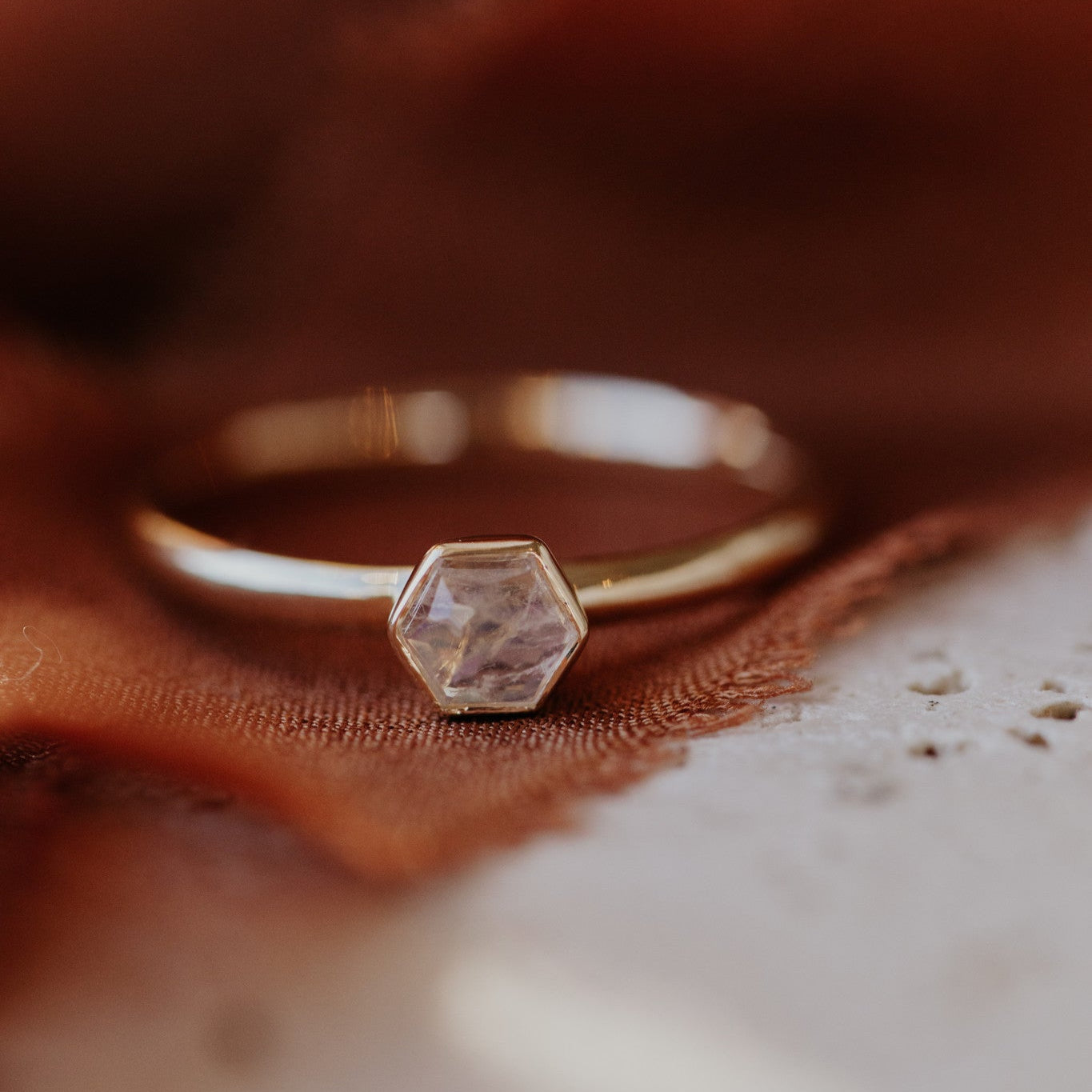 A 4mm tiny hexagon moonstone ring set in a high polish bezel, displayed on a brown textured surface.
