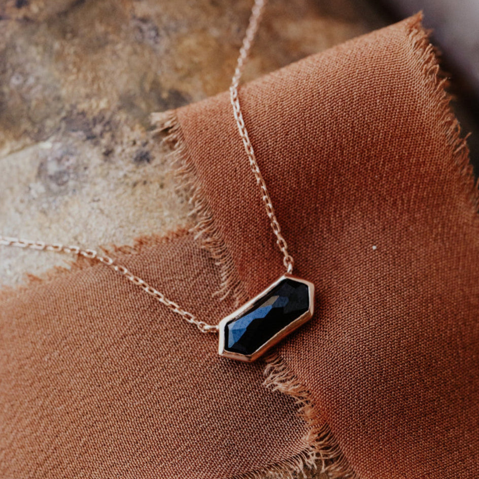 A long hexagon black spinel bezel necklace laid out on a brown textured surface.