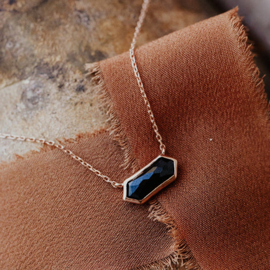 A long hexagon black spinel bezel necklace laid out on a brown textured surface.