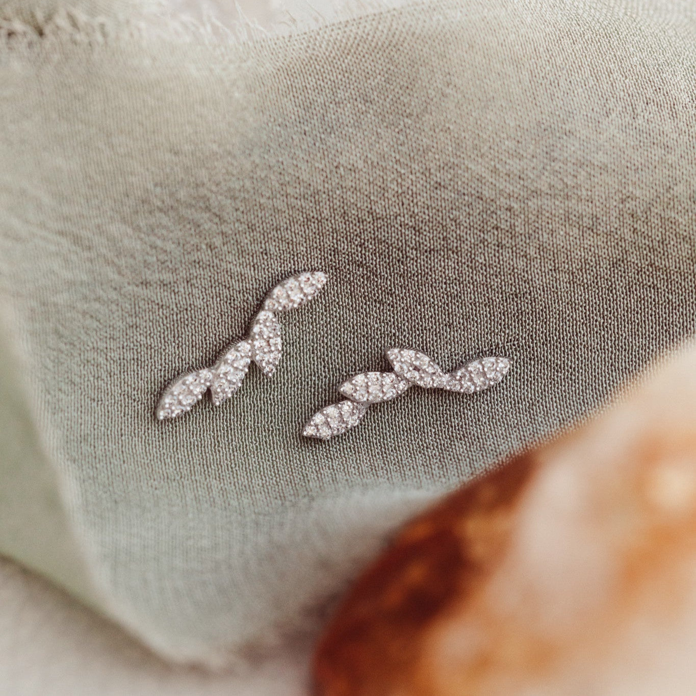Close-up of 14k gold stud earrings with marquise shapes set with pave diamonds, displayed on a textured surface.