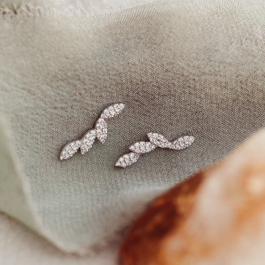 Close-up of 14k gold stud earrings with marquise shapes set with pave diamonds, displayed on a textured surface.