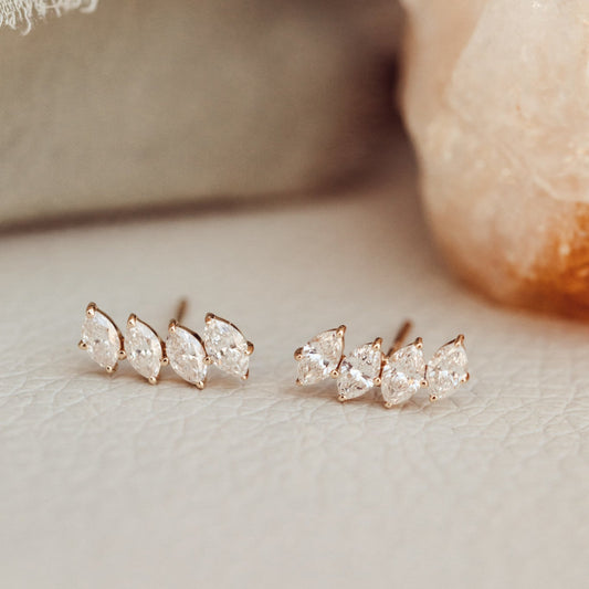 A pair of 14k gold stud earrings featuring four marquise shaped diamonds set in prongs, displayed against a neutral background.
