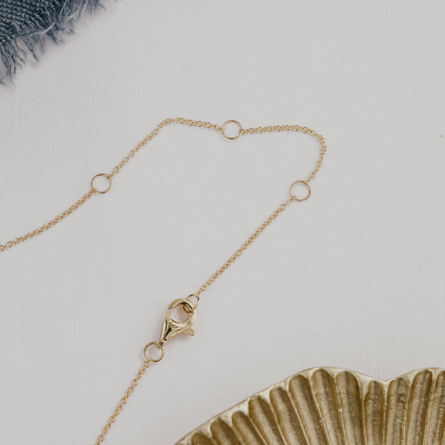 Gold necklace on a white surface with a ceramic plate and textured fabric.