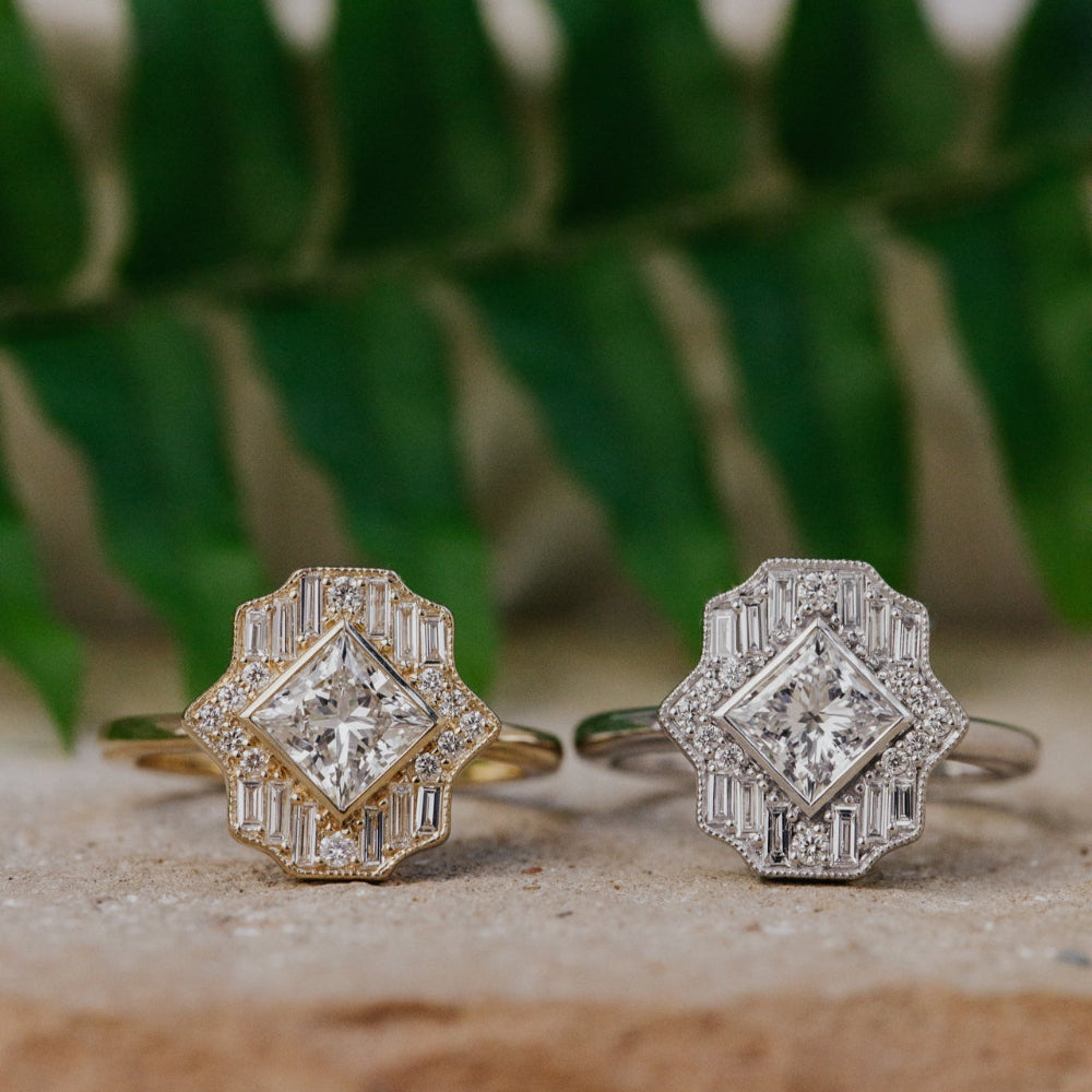 Two diamond halo rings on a stone surface with a blurred green leafy background