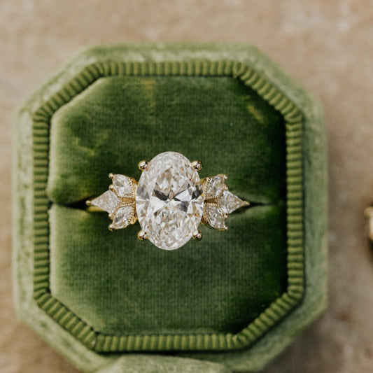 Oval diamond ring in a green velvet box on a textured surface