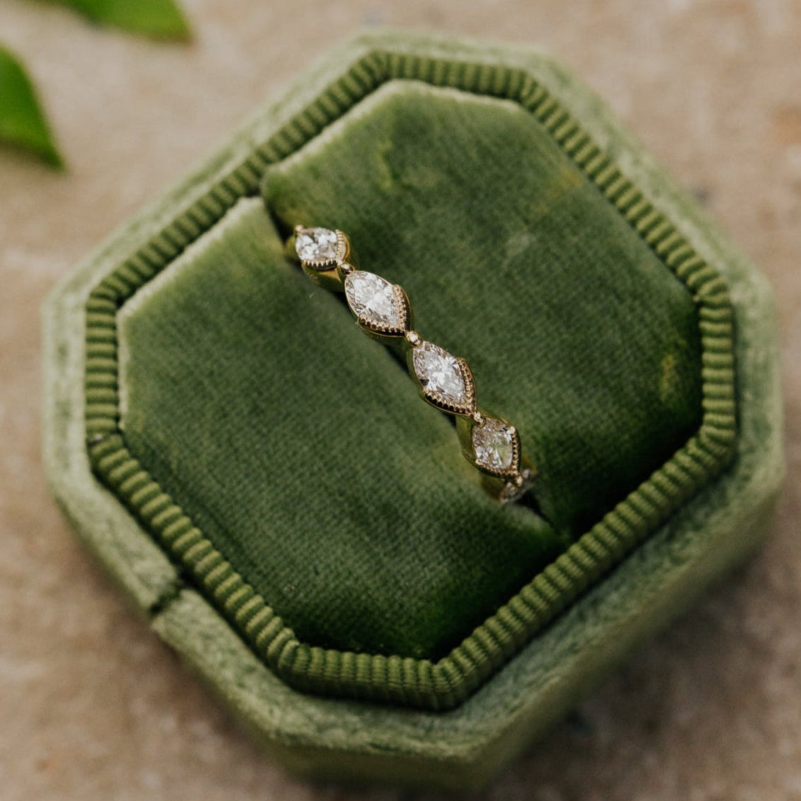 Marquise diamond band in a green velvet box on a textured surface with leaves.