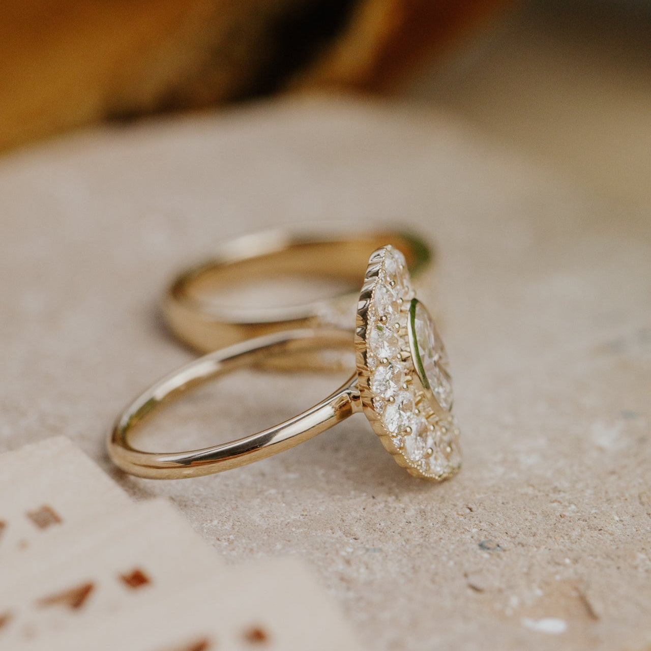 Two gold rings with diamond accents on a textured surface.