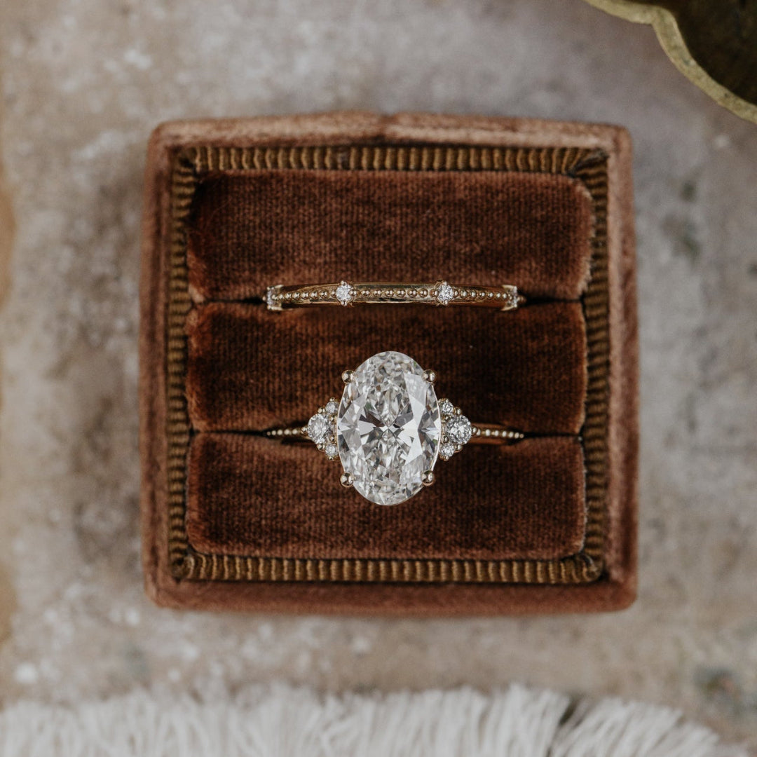 Oval diamond ring in a brown velvet box on a textured surface