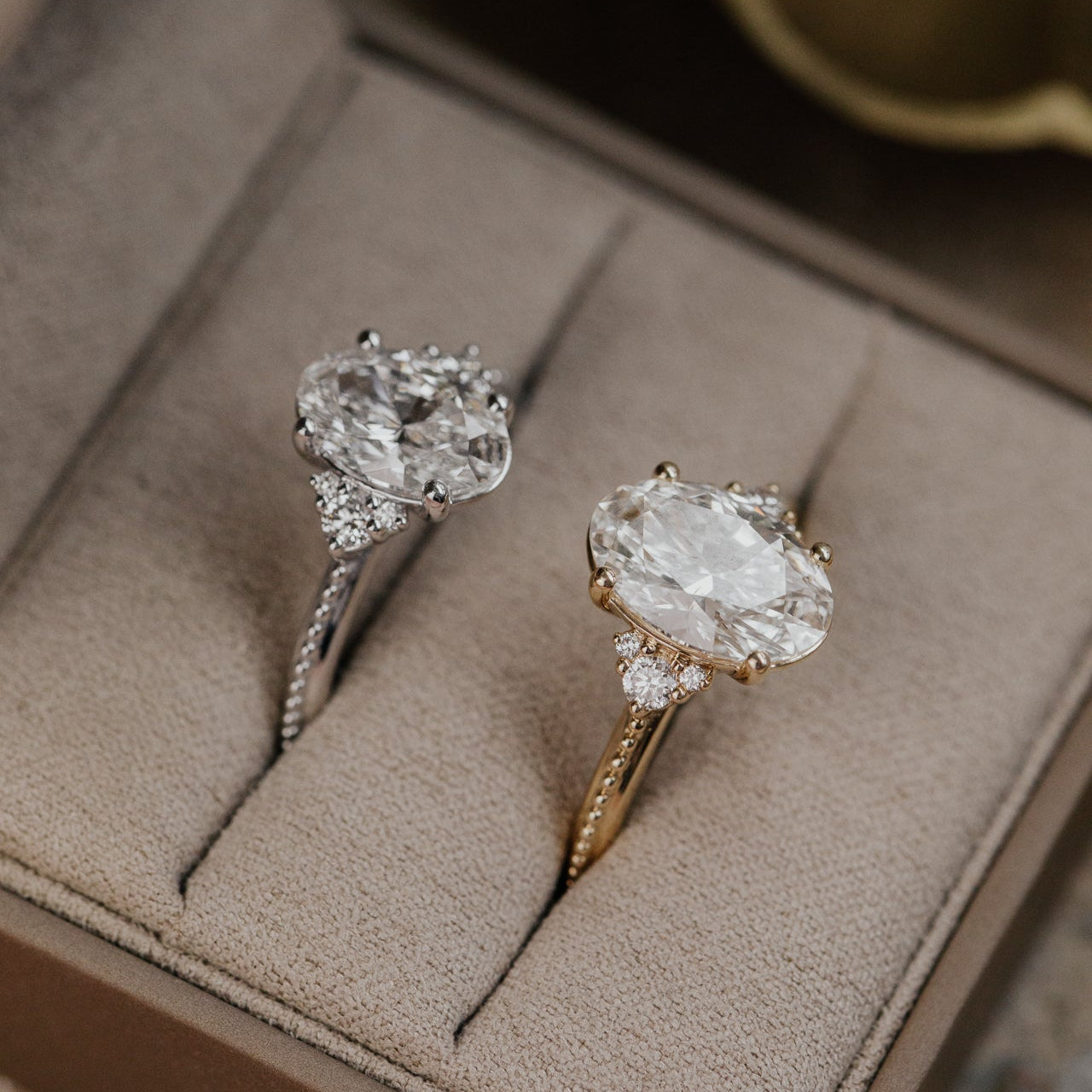 Two oval diamond rings in a jewelry box with a blurred background