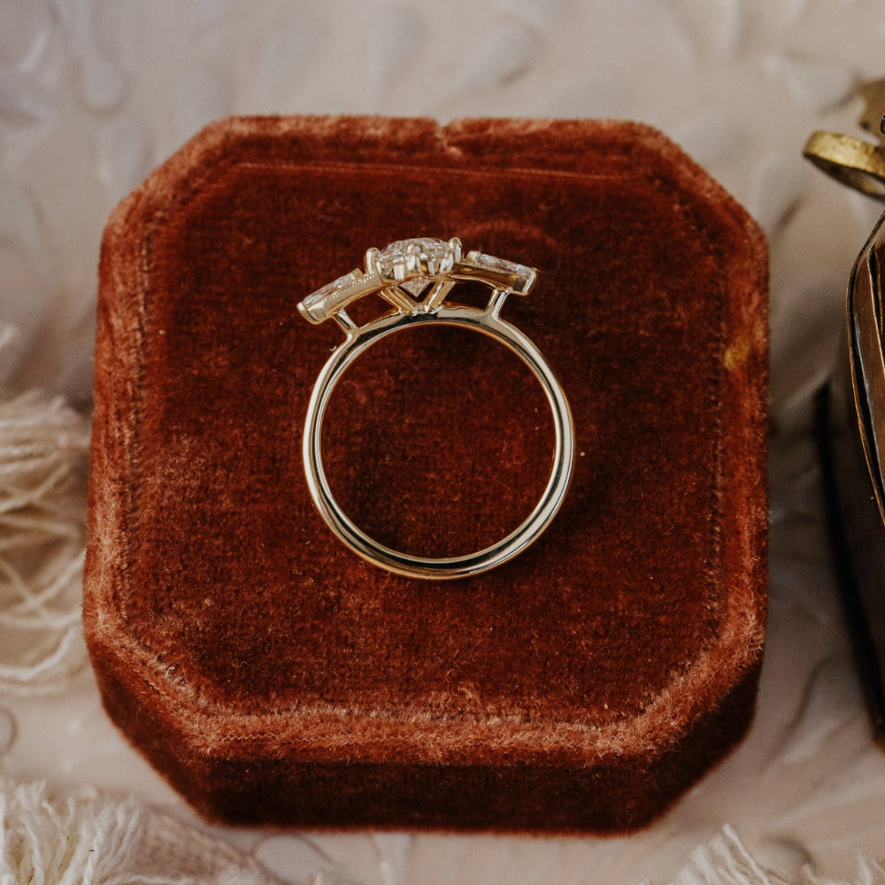 gold ring with a diamond on a brown velvet box against a textured beige background