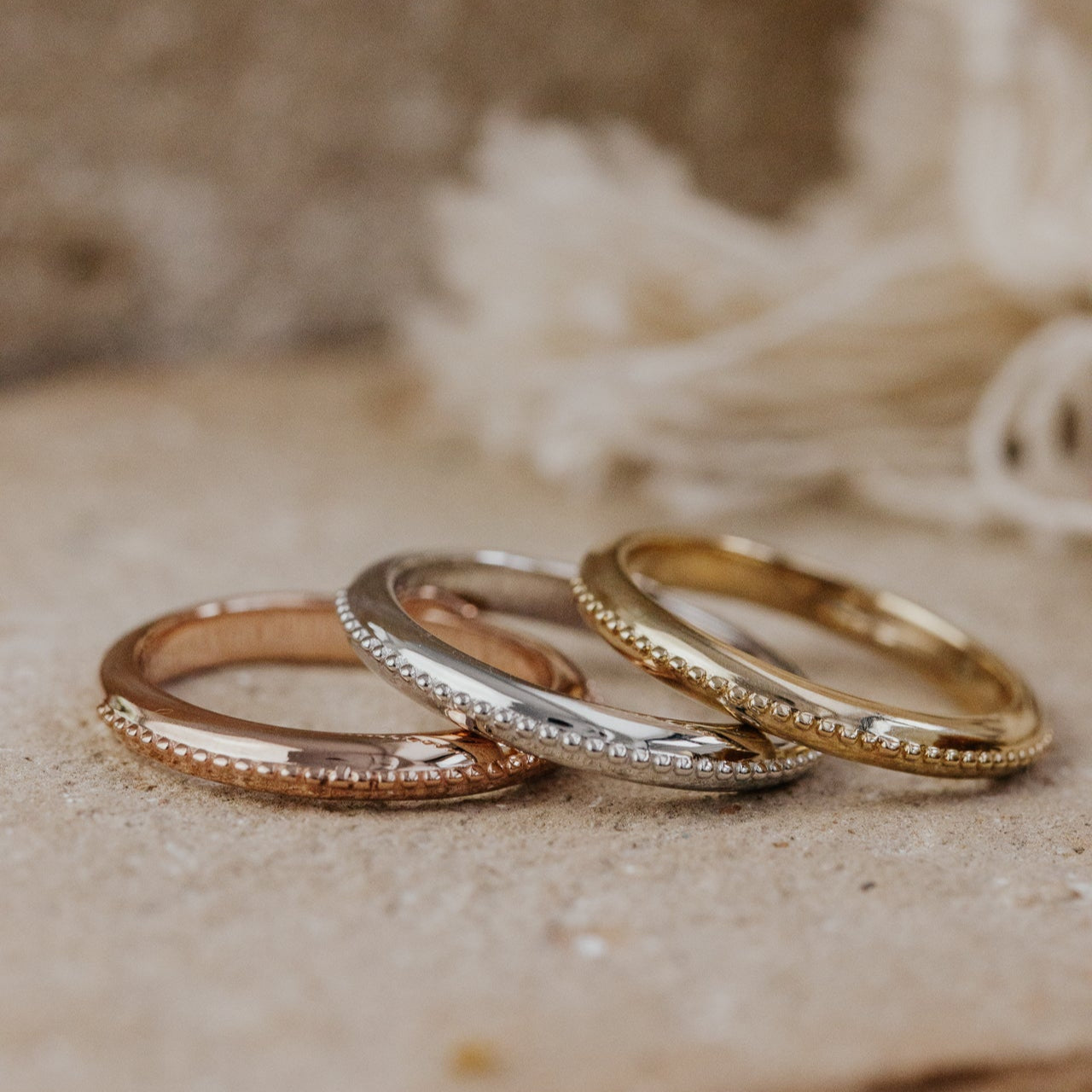 Three gold rings stacked on a textured surface with a blurred natural background