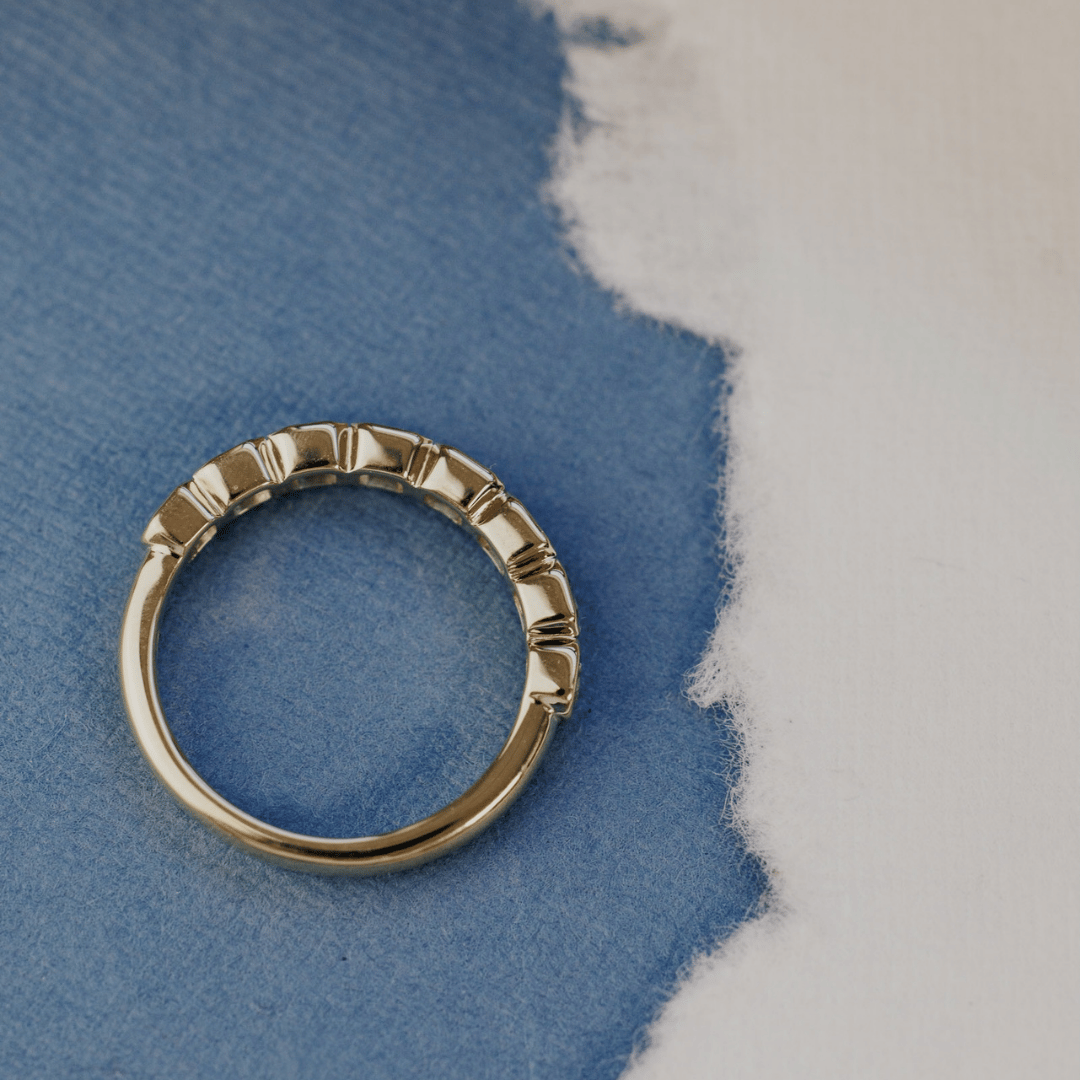 A 14k gold ring featuring asscher cut, blue sapphire gemstones, show from an ariel view, displayed on a blue surface with a soft-focus background.