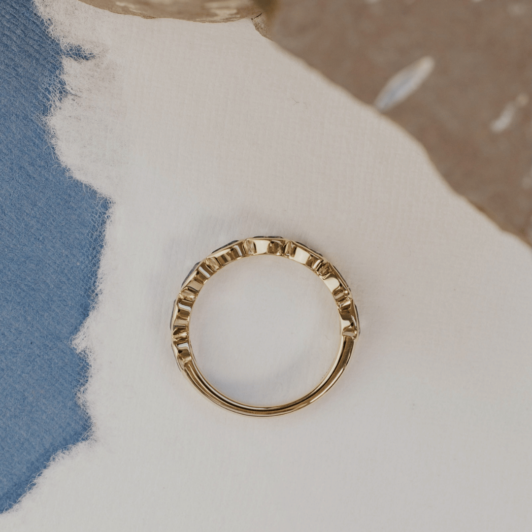 A 14k gold ring featuring blue pear sapphire gemstones displayed on a white surface with a soft-focus background from an ariel POV.