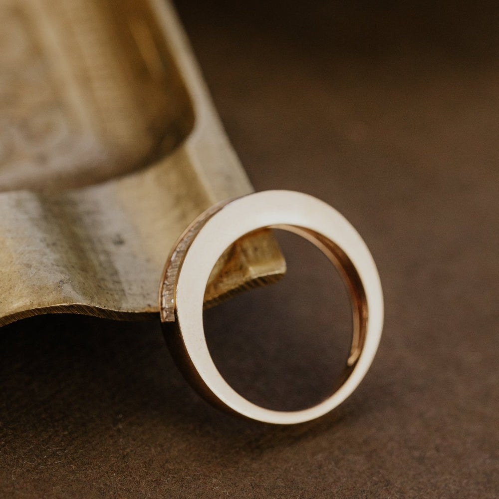 Close-up of a rose gold wedding band on a textured brown surface.