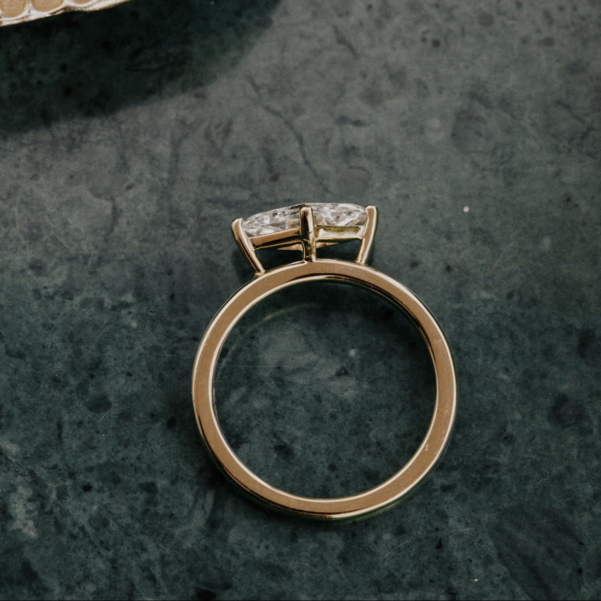 Gold ring with a diamond on a dark textured surface.