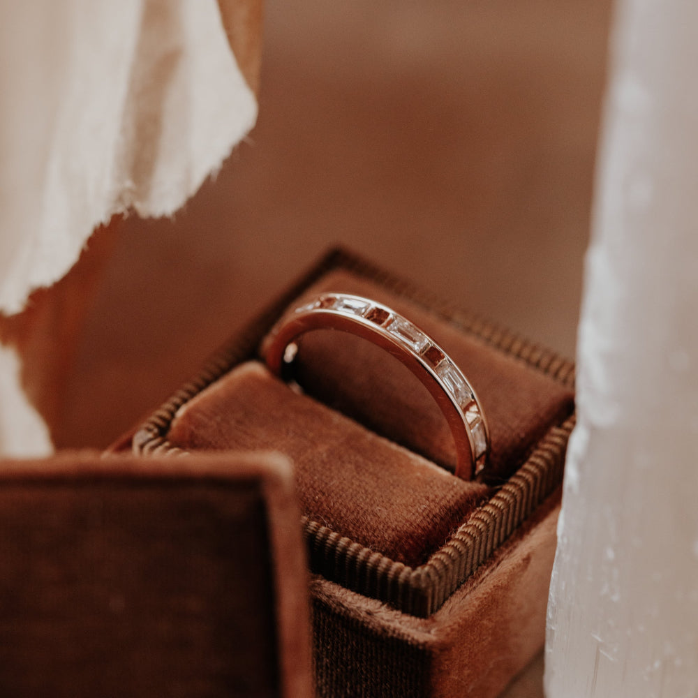 White gold wedding band with diamonds in a brown jewelry box.