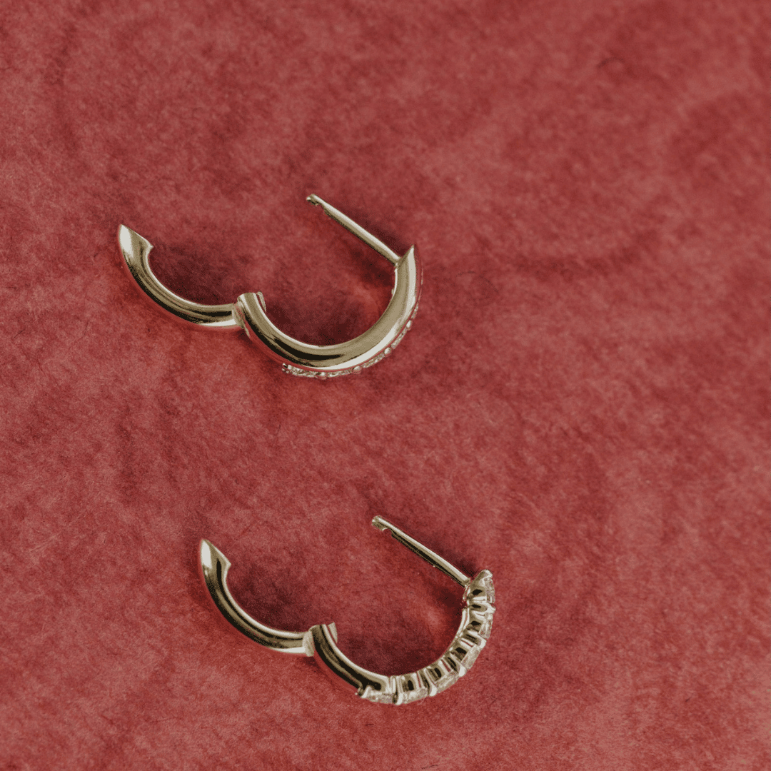 14k gold diamond huggie earrings showcased on a textured red surface.