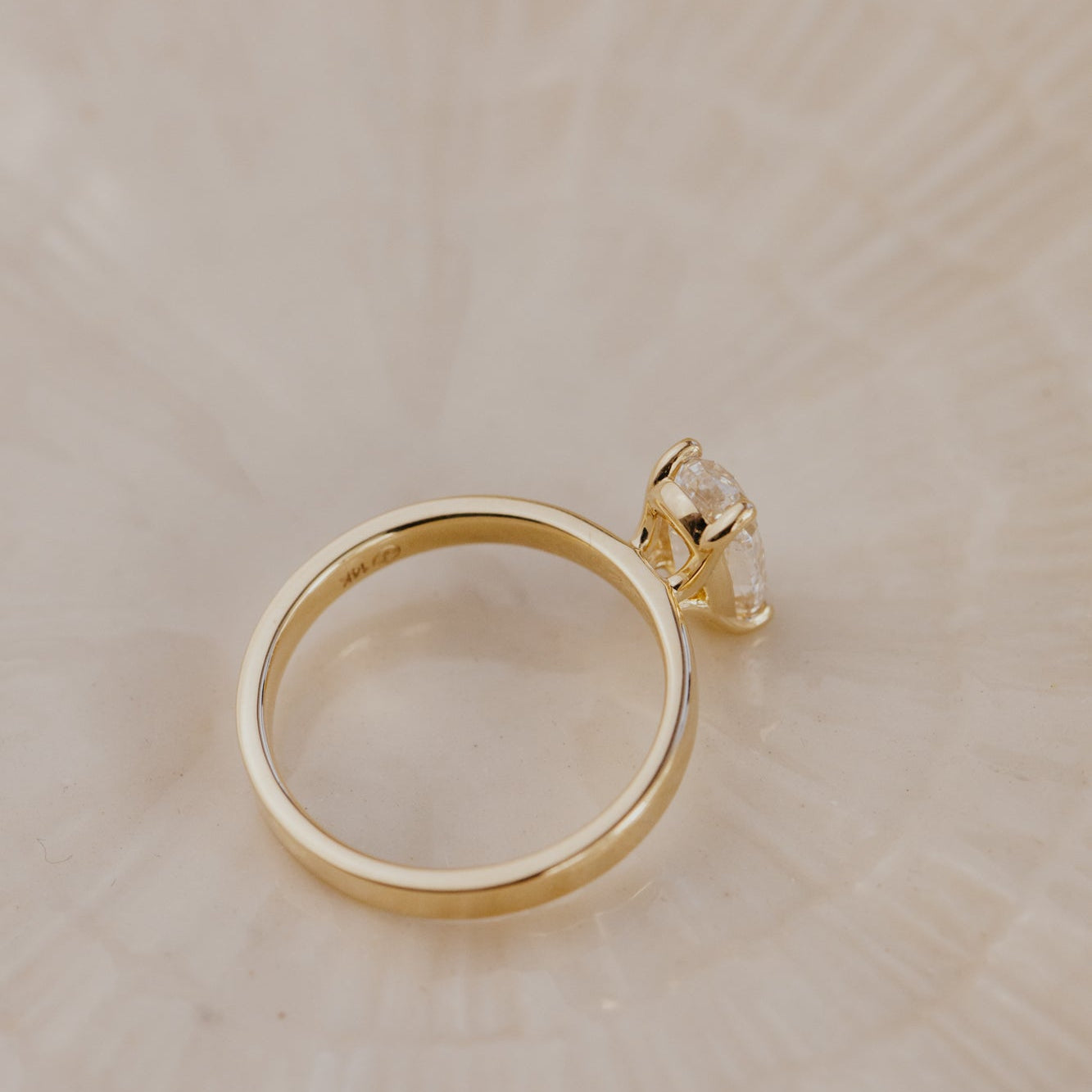 Gold Octavia ring with a diamond on a beige surface.
