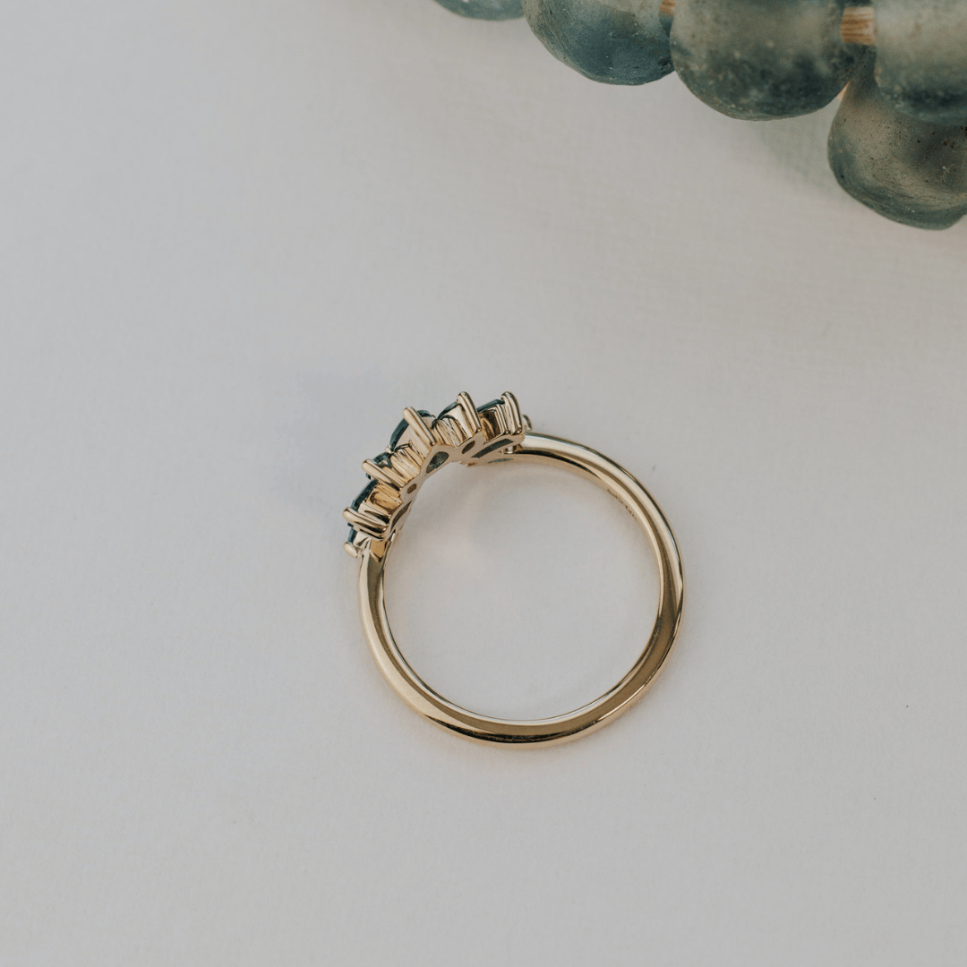 A 14k gold band-style ring with multiple sapphire stones set in a starburst design, shown from an ariel POV.