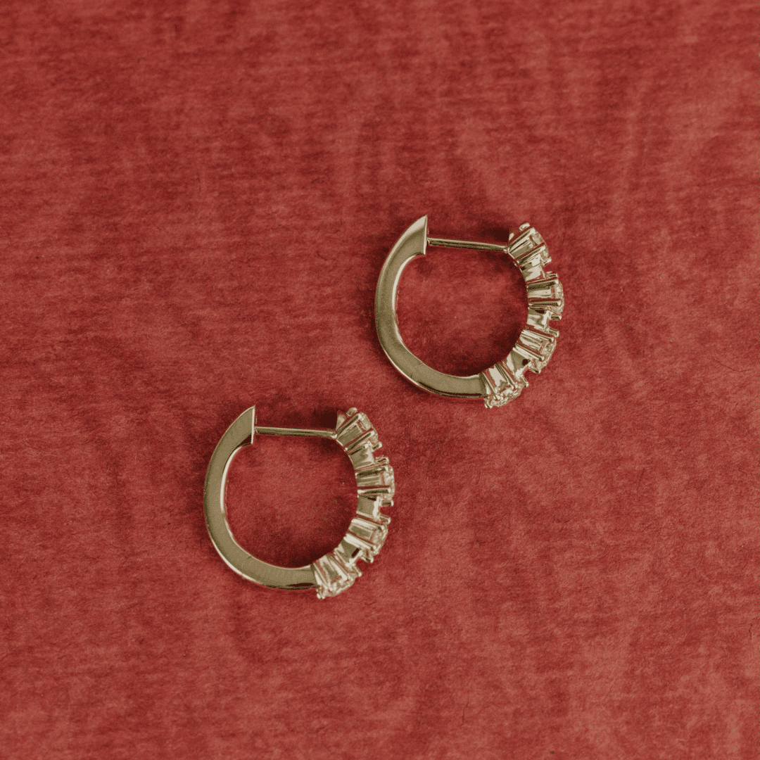 14k gold diamond 4-prong huggie earrings set showcased on a textured red surface.