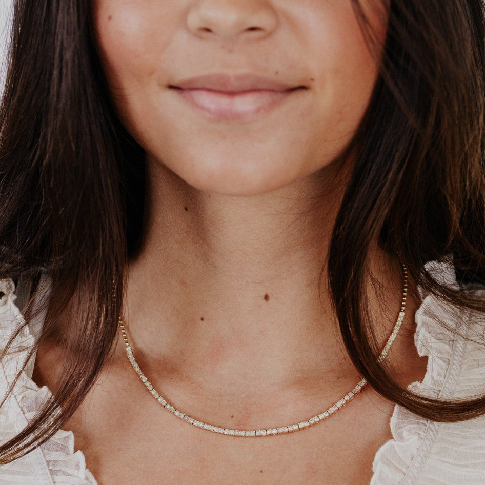 Close-up of a woman wearing a delicate opal necklace with a blurred background