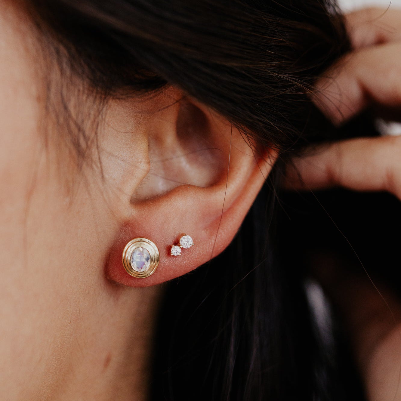 Close-up of an ear with gold earrings and a hand adjusting hair.