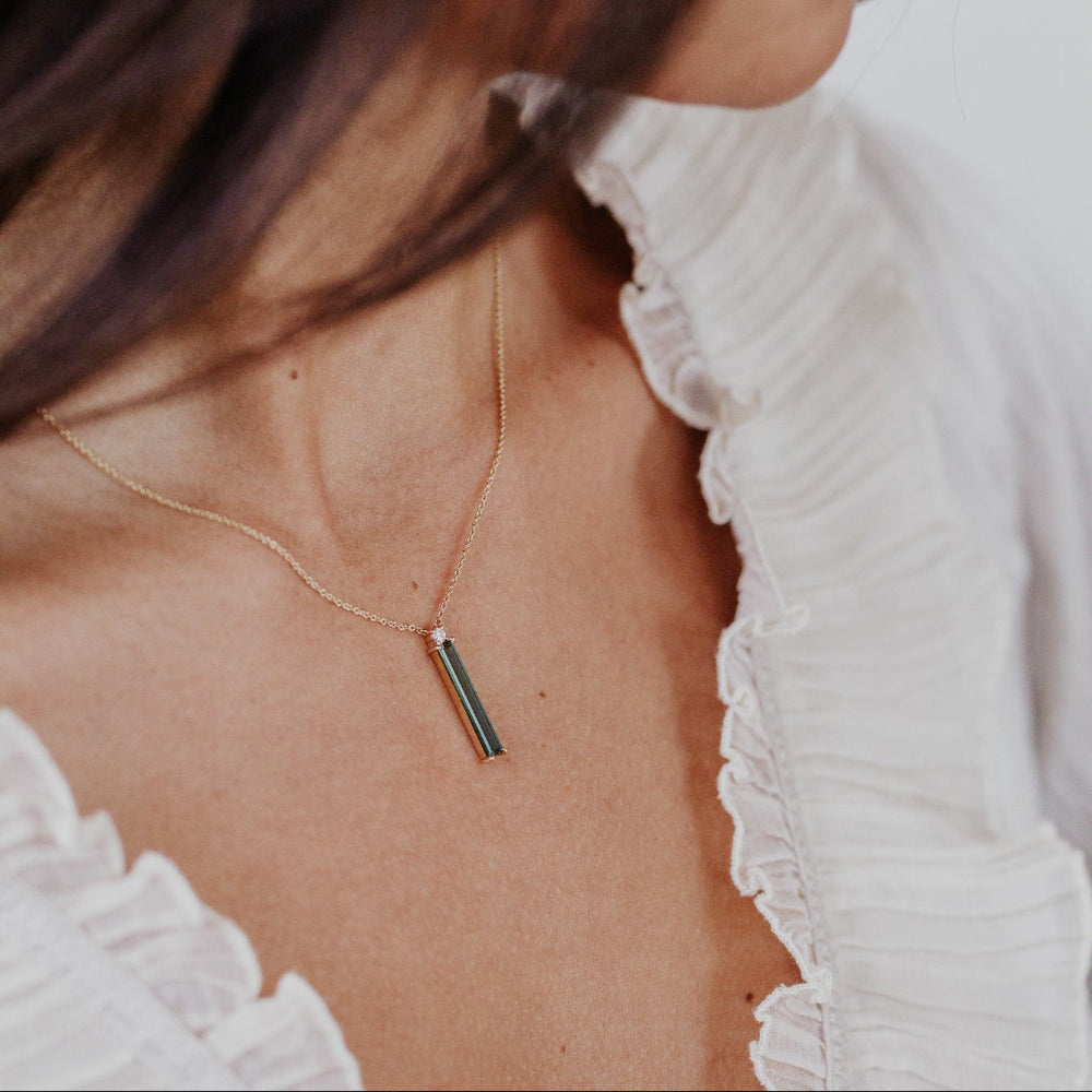 Necklace with a cylindrical green tourmaline pendant worn by a person in a white top.