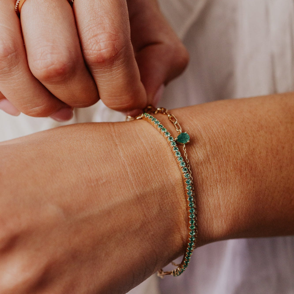 Close-up of a hand wearing gold rings and a green emerald bracelet on a blurred background