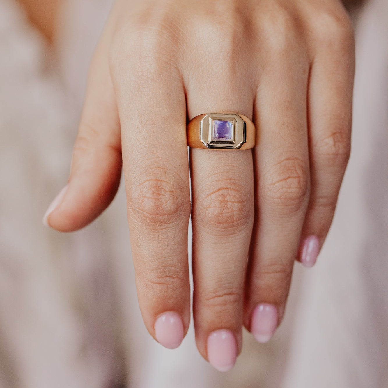Yellow gold ring with a purple gemstone on a hand against a neutral background