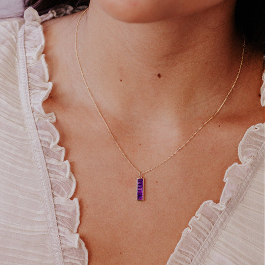 Close-up of a person wearing a necklace with a small amethyst purple pendant.
