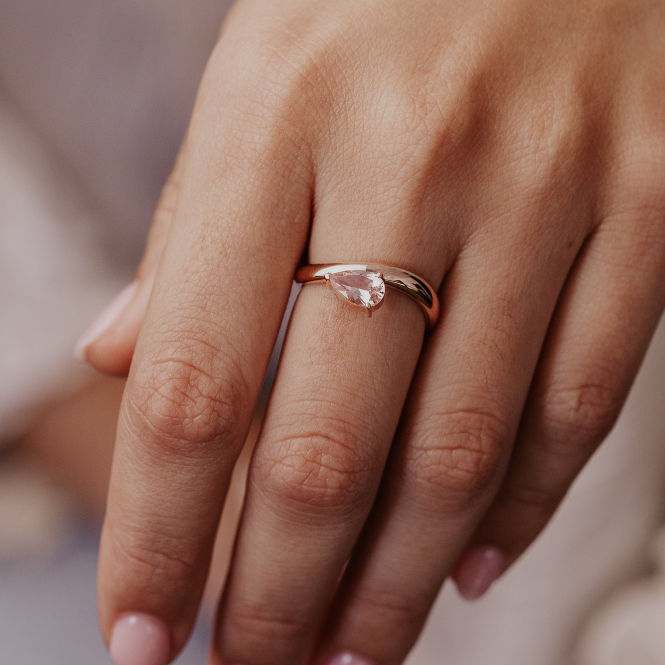 Close-up of a hand wearing a rose gold ring with a clear stone.