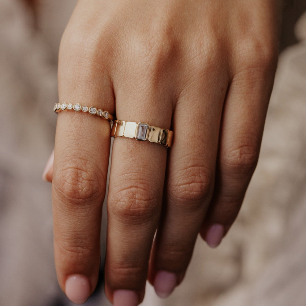 Close-up of a hand wearing two gold rings with a blurred background