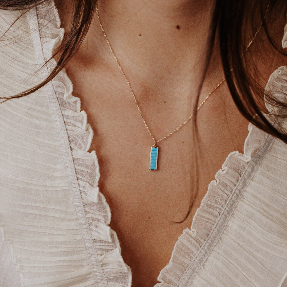 Necklace with a blue Turquoise pendant worn by a person in a white blouse.