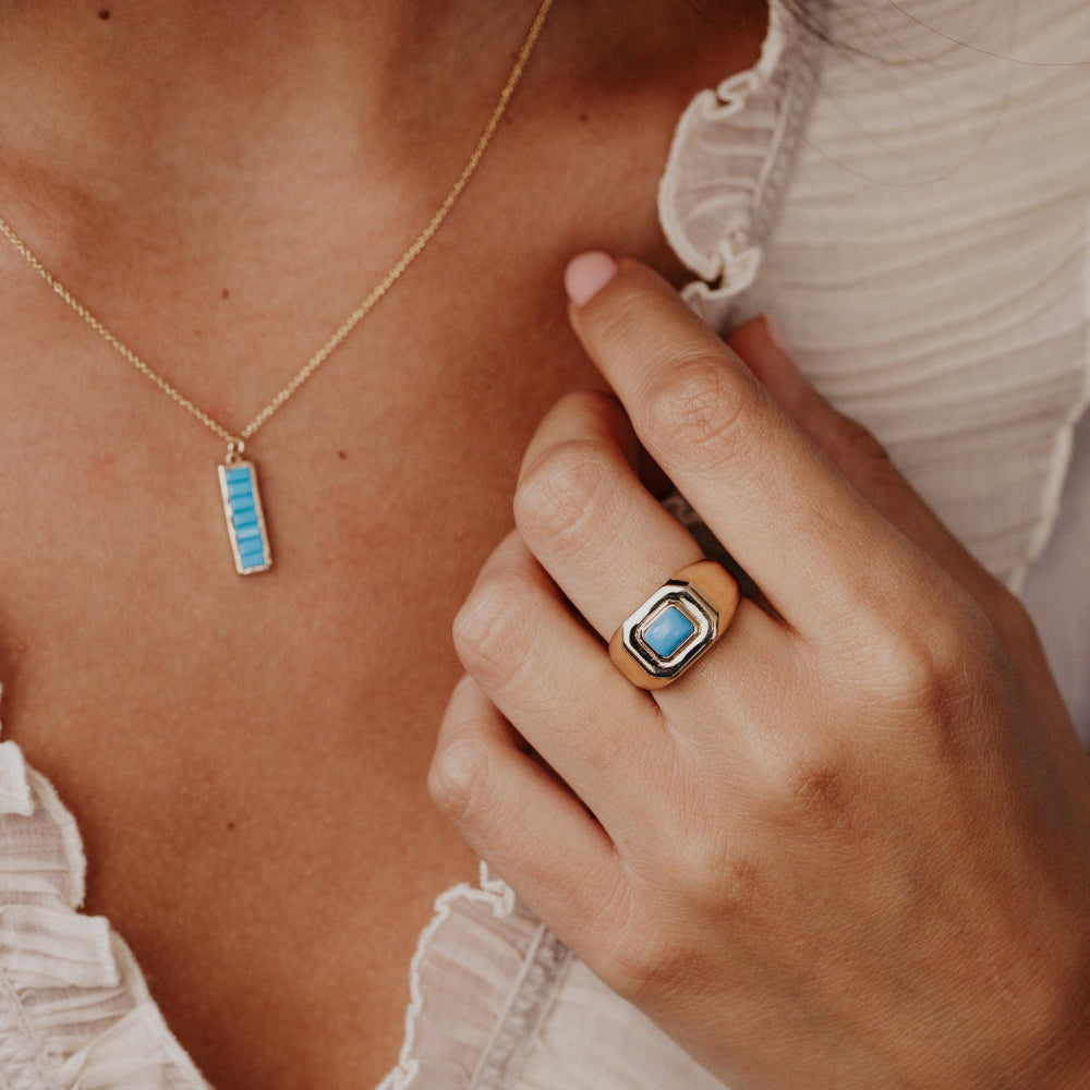 Close-up of a person wearing a gold necklace with a blue pendant and a matching ring.