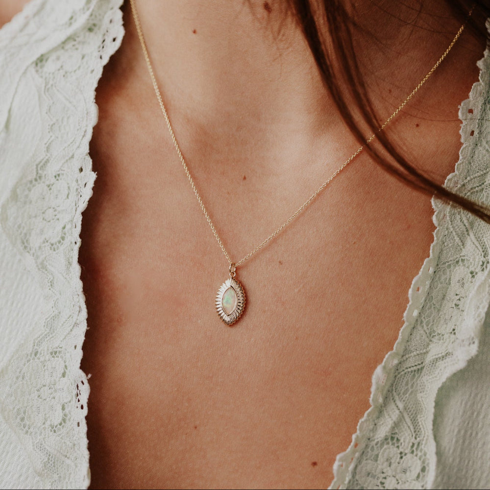Close-up of a necklace with a opal pendant on a person wearing a light green lace top.