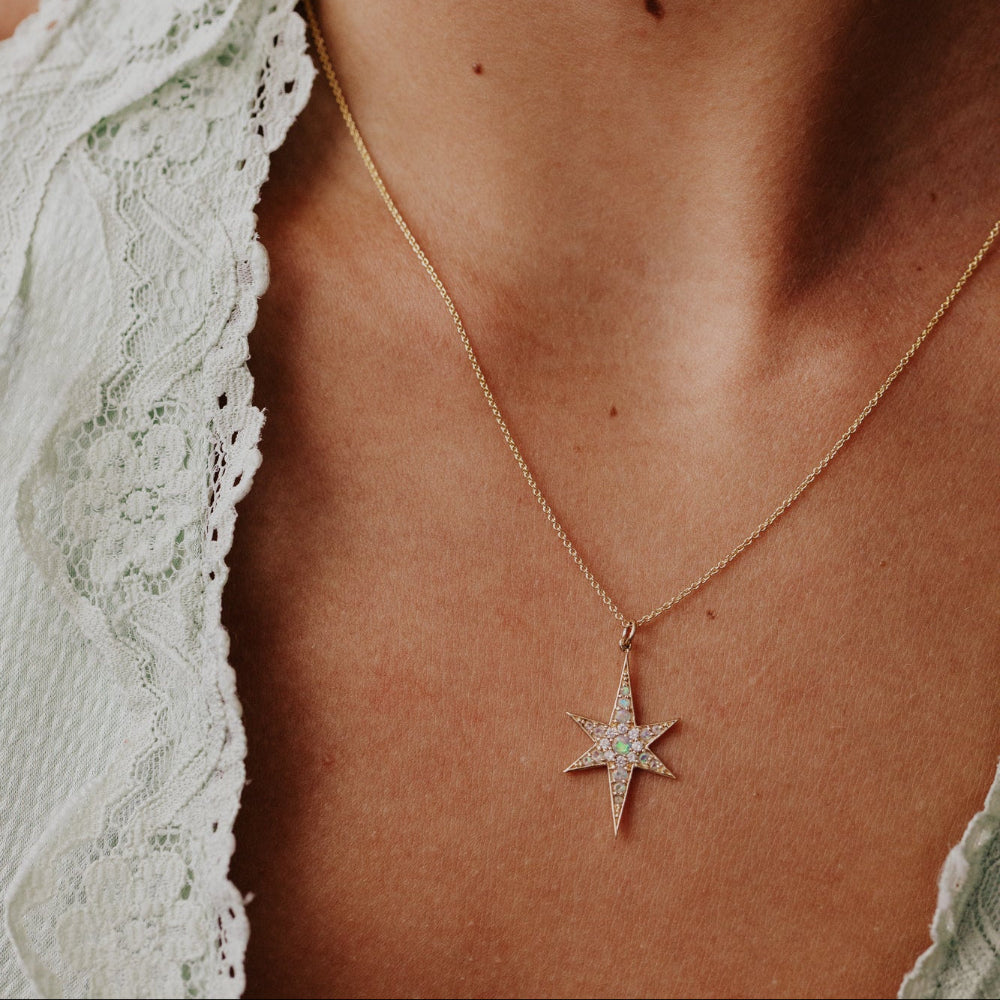 Star-shaped necklace with a opal and diamind gemstone on a person wearing a white lace garment.