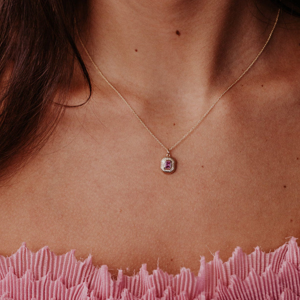 Necklace with a pink sapphire pendant worn by a person, focusing on the jewelry.