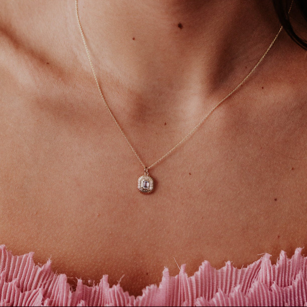 Necklace with a green amethyst pendant on a person's neck against a pink textured background