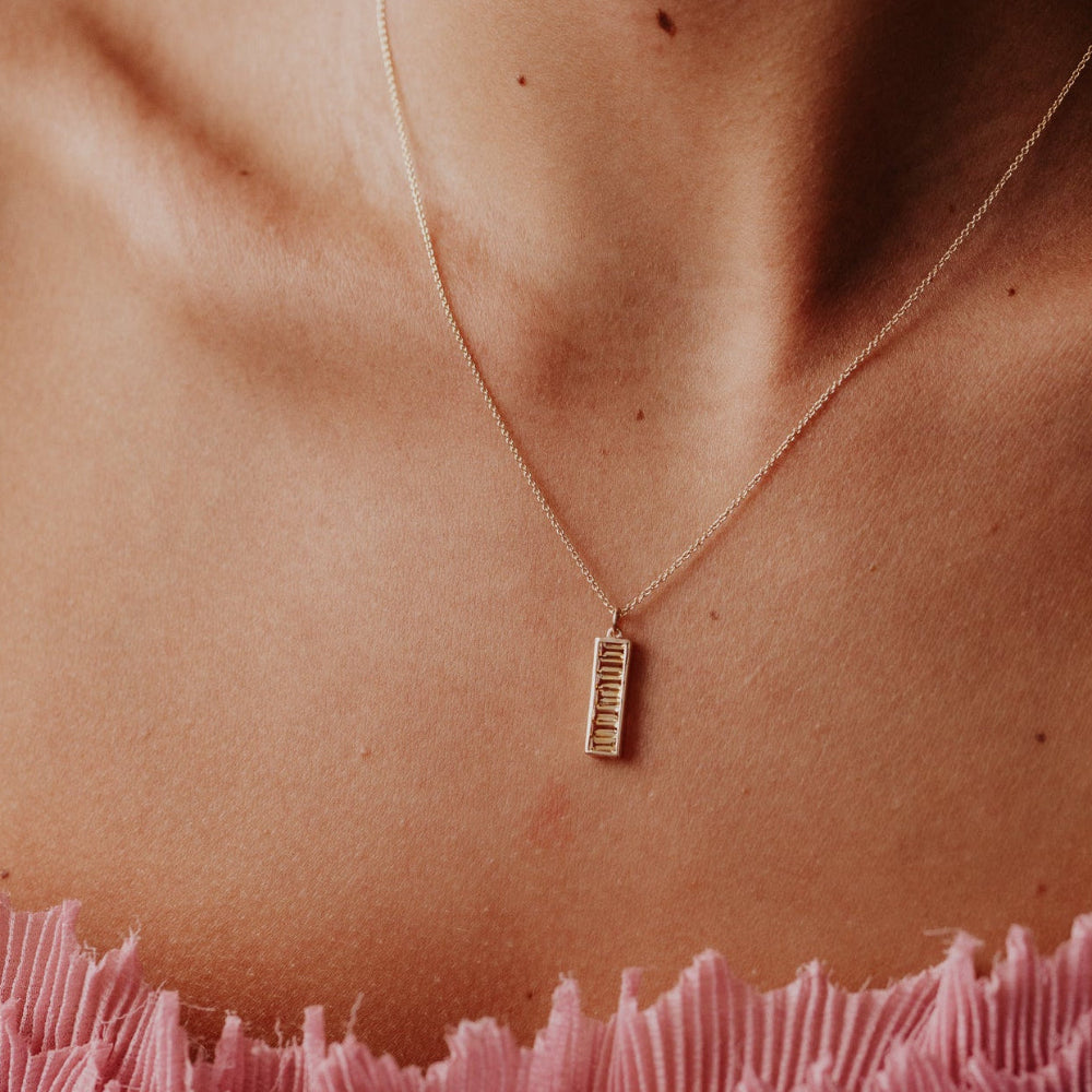 Necklace with a small Citrine pendant worn by a person with pink fabric in the foreground