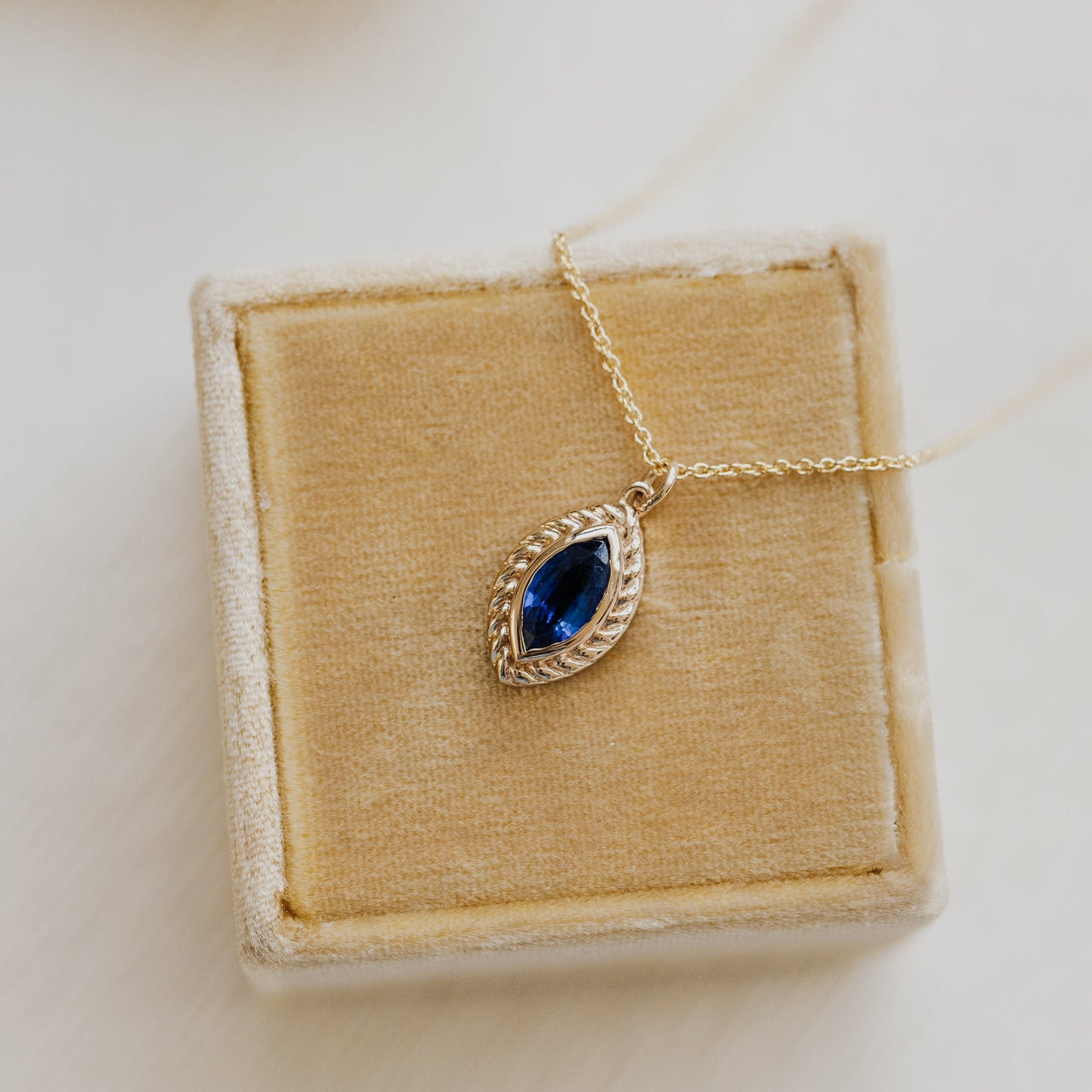Gold necklace with a blue Kyanite gemstone on a beige jewelry box