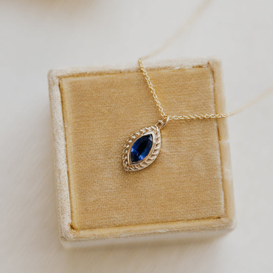 Gold necklace with a blue Kyanite gemstone on a beige jewelry box