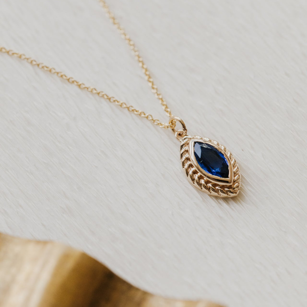 Gold necklace with a blue Kyanite gemstone pendant on a light background